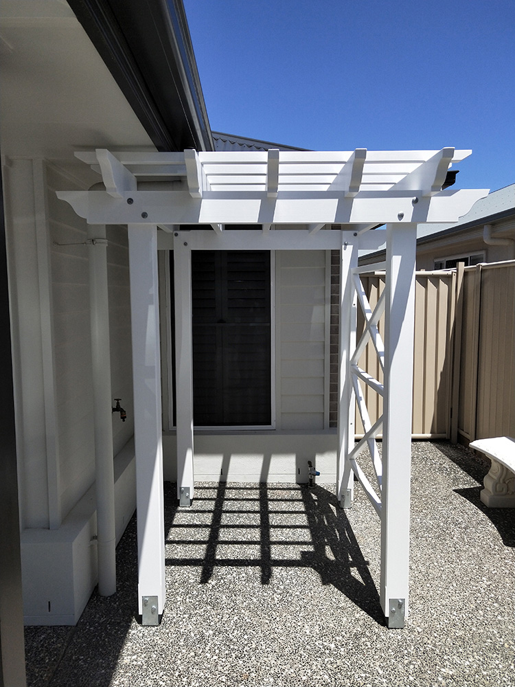 This painted white Pergola has been set into the corner of the residence, adding depth and a complimenting feature to this sitting area where a bench will be placed.