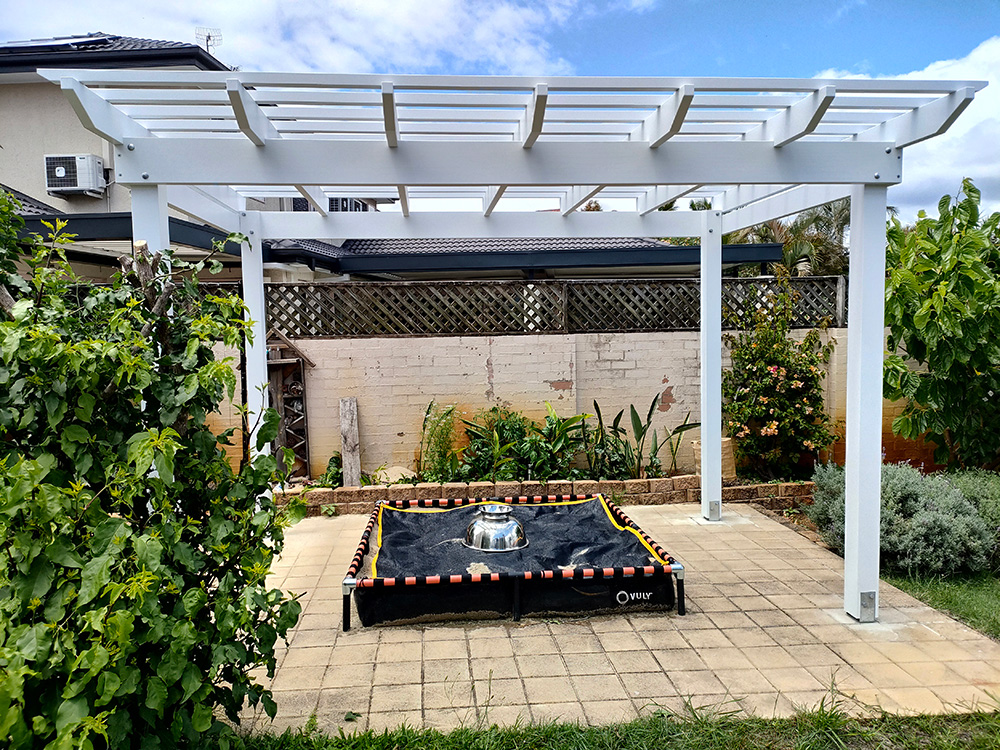 This white painted Pine Pergola sits overop of an existing concreted and paved area.