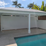 Front view of the white Pool Cabana showing its hip roof, full rear wall, half side wall and Decorative Post Boxes.