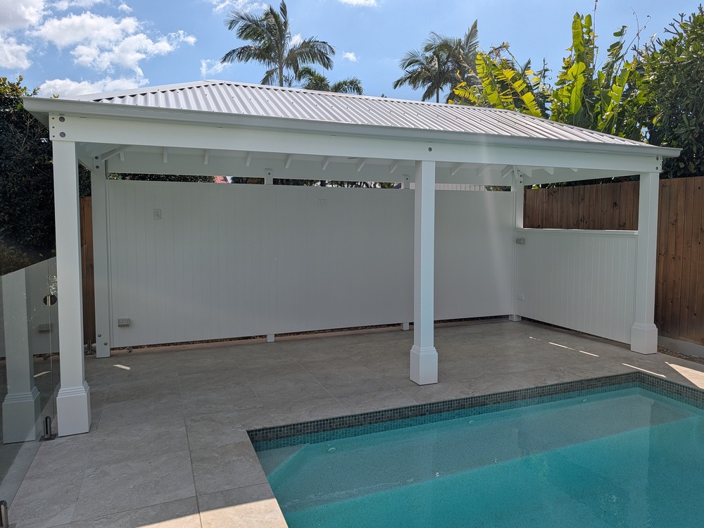 Front view of the white Pool Cabana showing its hip roof, full rear wall, half side wall and Decorative Post Boxes.