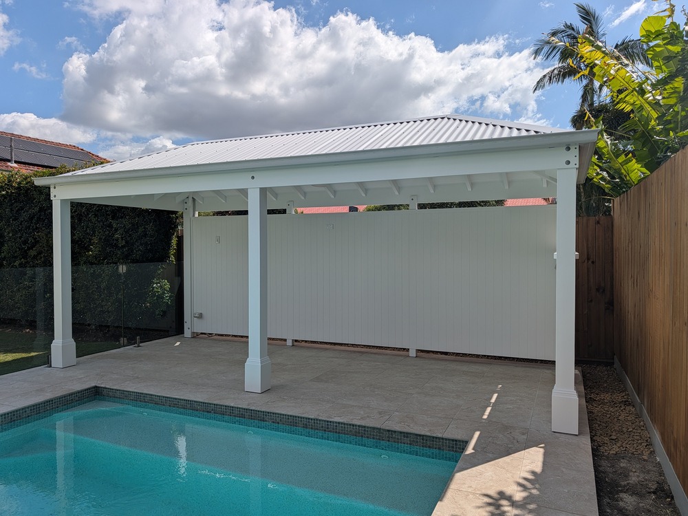 Angled view of the white hip roof Pool Cabana showing its metal roof, gutter, rear wall and front posts.