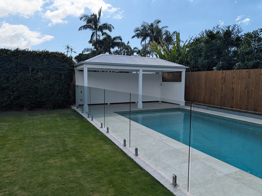 White hip roof Pool Cabana with rear and side walls beside a swimming pool and glass pool fence.