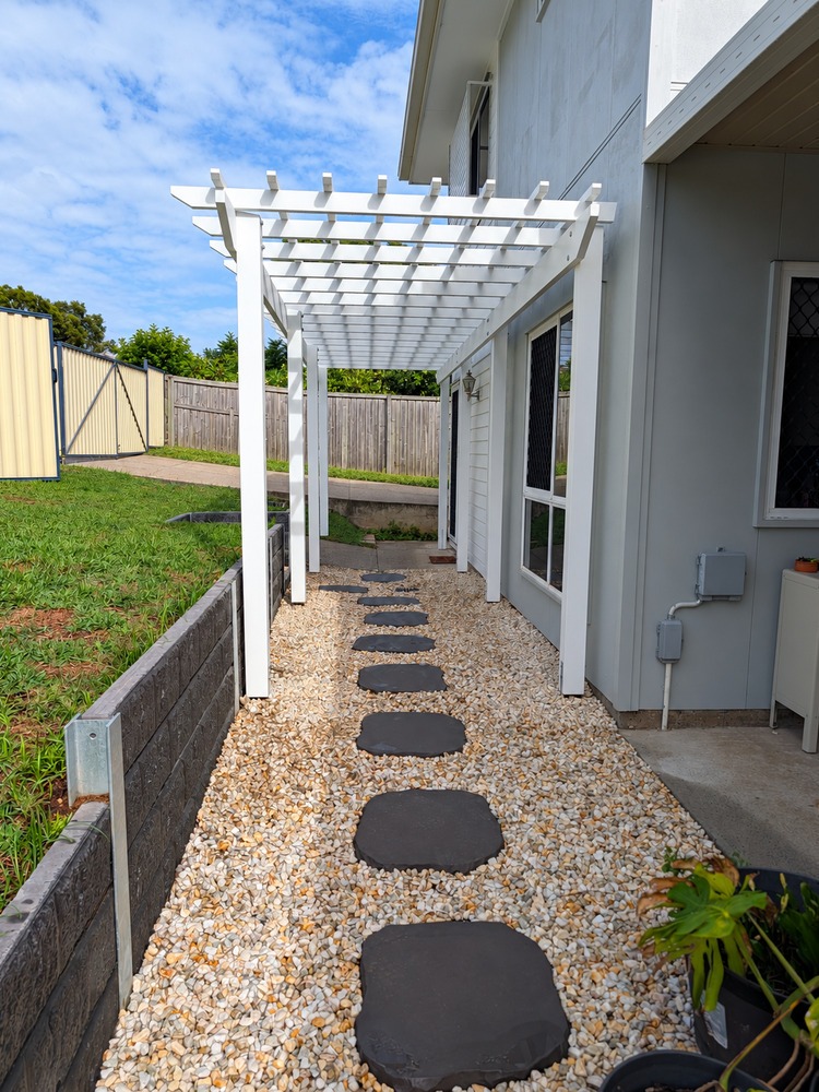 White Traditional Pergola framing a landscaped walkway with stepping stones.