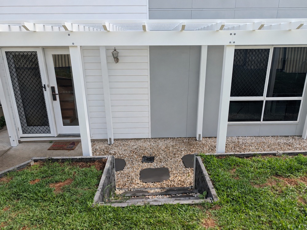 White Traditional Pergola framing the entrance beside garden steps and retaining walls.