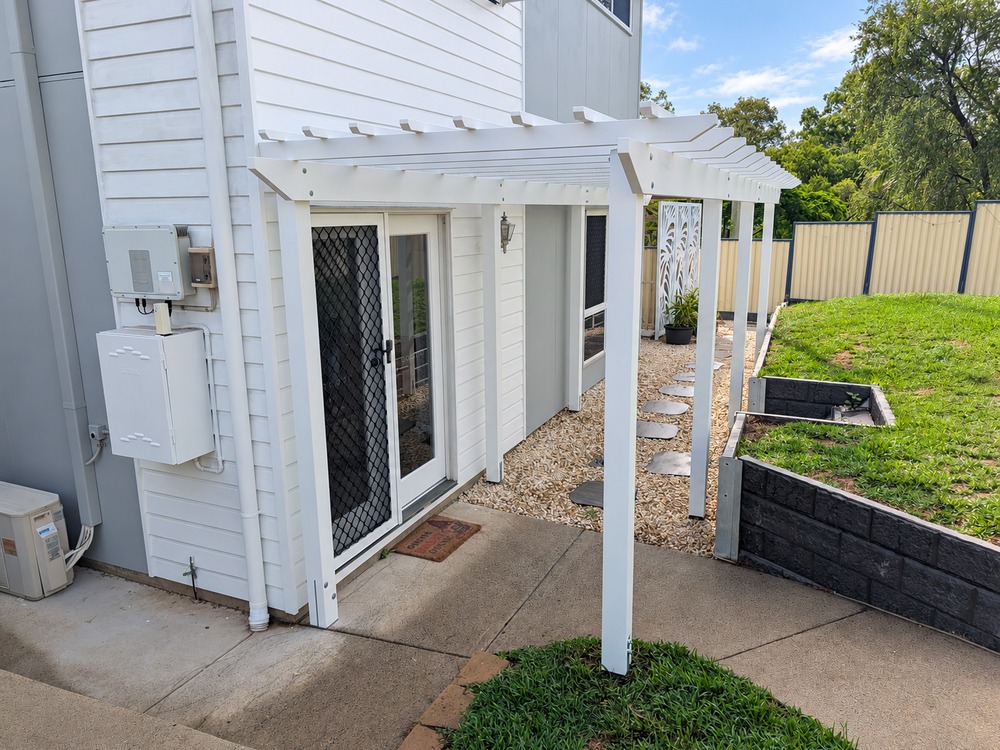 White Traditional Pergola framing the front entrance beside the house.
