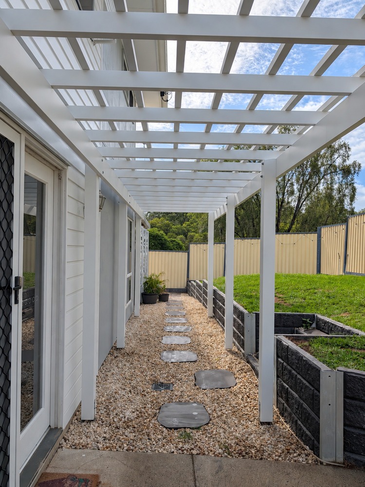 View beneath a white Traditional Pergola along the landscaped garden walkway.