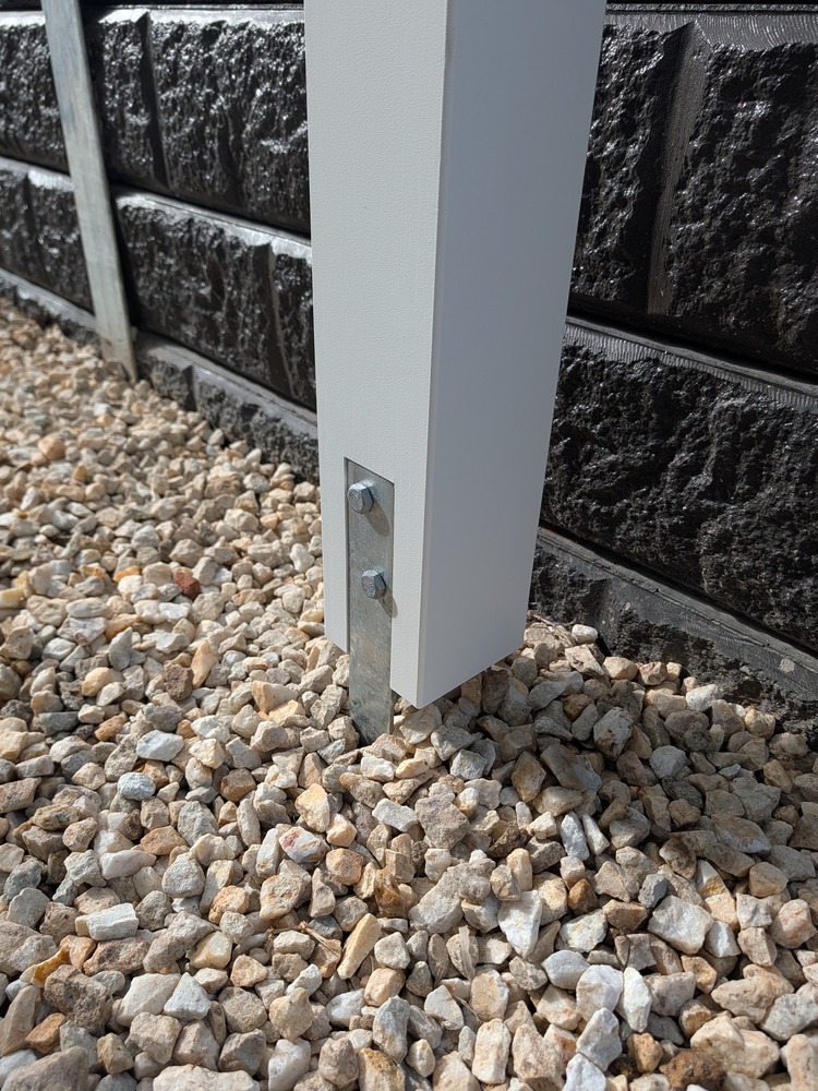 White Pergola post fixed with a galvanized ground anchor beside the retaining wall.