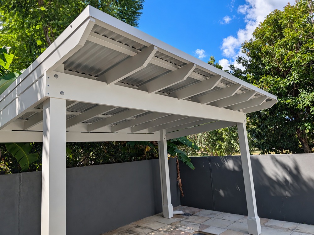 White painted beams and exposed timber rafters beneath the skillion Colorbond roof of a poolside pergola.