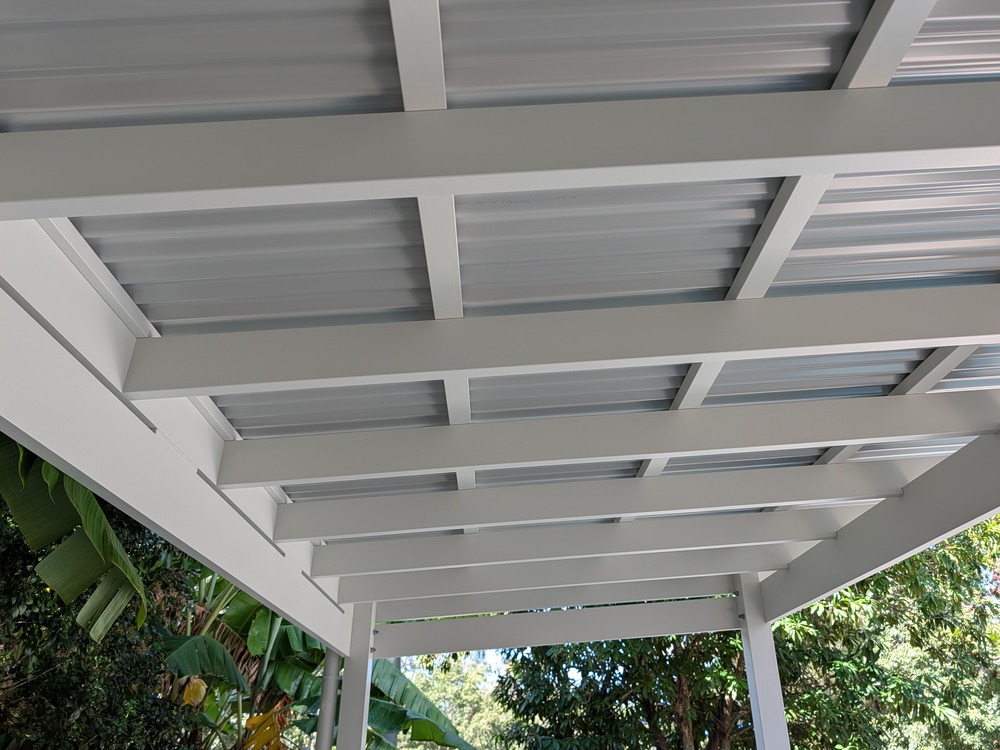 White timber rafters and battens beneath the corrugated Colorbond roof, viewed from inside the pergola.