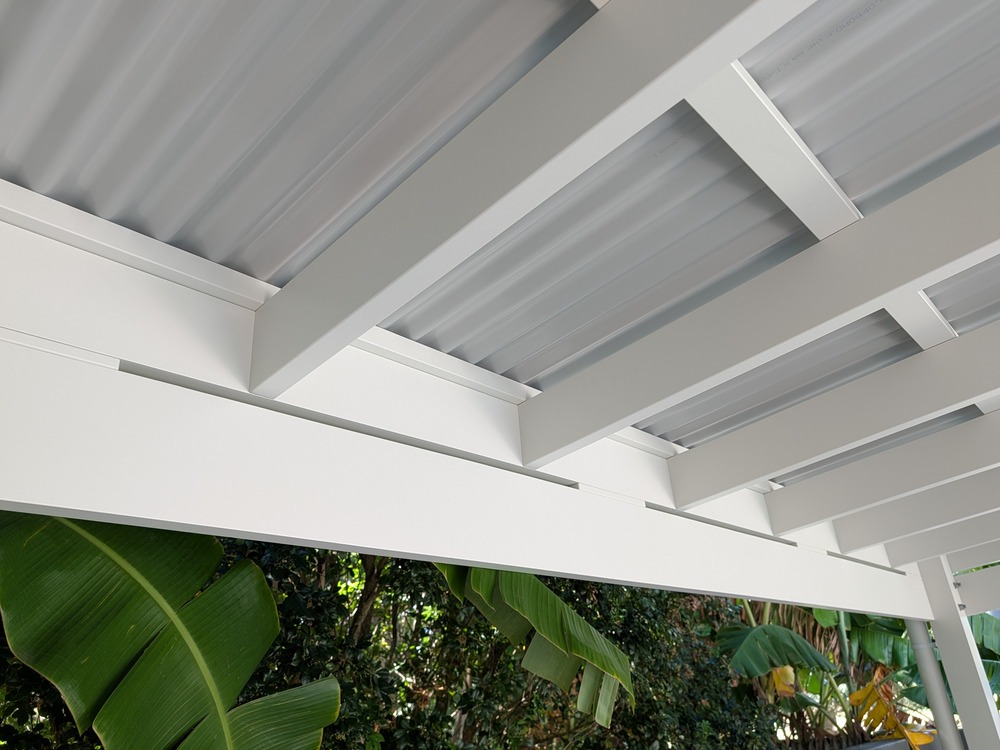 Close view of white painted timber beams and rafters beneath the pergola's Colorbond roofing.
