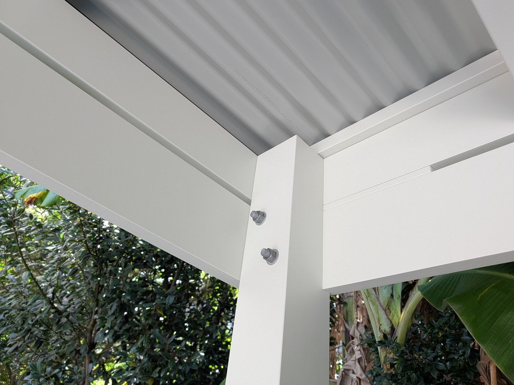 Close view of a white laminated Pine post and painted beam connection with visible galvanized bolts.