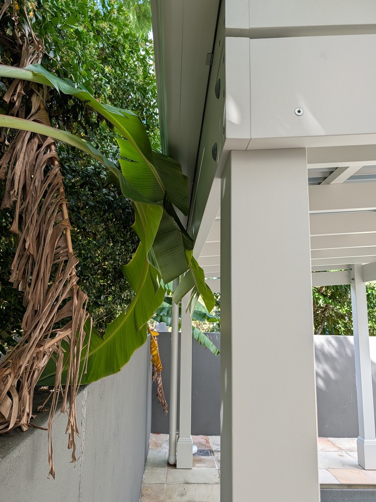 White painted pergola post and beam viewed along the tiled pool surround.