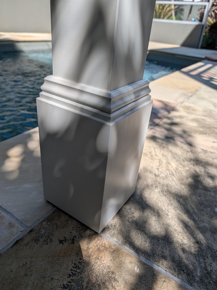 White Decorative Post Box with stepped trim at the base of a pergola post on the tiled pool surround.